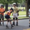 A group of people of various ages and skill levels receive instruction from a coach during an inline skating lesson at a local rink.