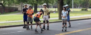 A group of people of various ages and skill levels receive instruction from a coach during an inline skating lesson at a local rink.
